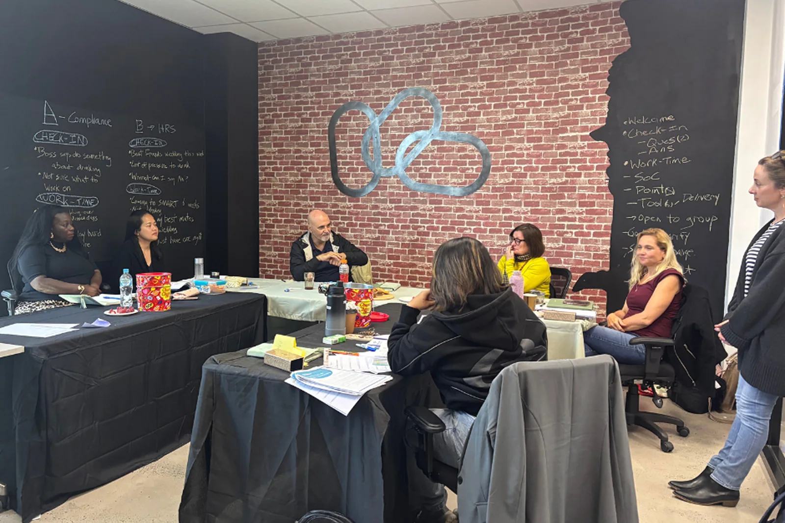 A TOIP session in progress, participants seated around tables with the week's agenda on the blackboard behind them